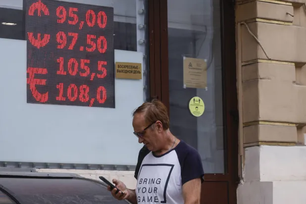 رجل يمر أمام شاشة في العاصمة الروسية موسكو تعرض سعر الروبل مقابل العملات الأجنبية... والذي بلغ الأربعاء أدنى مستوياته منذ مارس 2022 (إ.ب.أ)