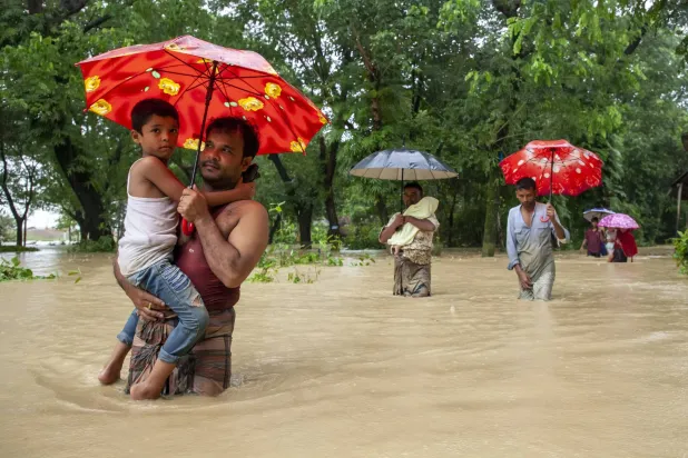 رجل يحمل ابنه ومظلة محاولاً العبور وسط المياه التي غمرت شوارع شيتاغونغ في بنغلاديش (د.ب.أ)