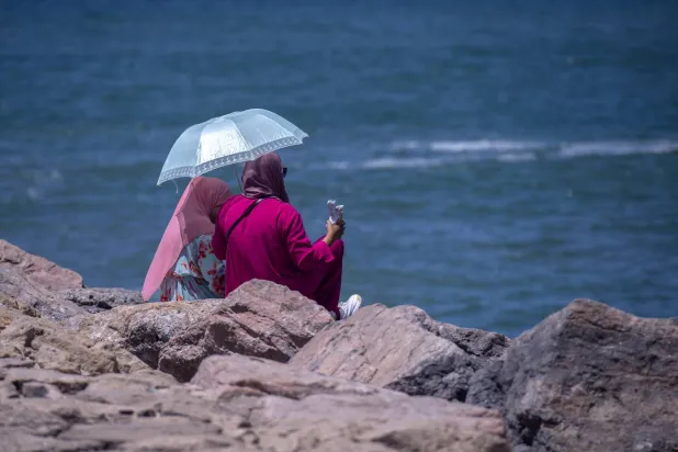 سيدتان تجلسان على الشاطئ تحت مظلة مع ارتفاع درجة الحرارة في الرباط، 9 أغسطس 2023 (إ.ب.أ)