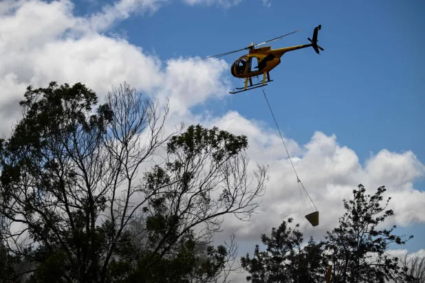 طائرة هليكوبتر لمكافحة الحرائق تلقي بالمياه بينما يقوم رجال الإطفاء في مقاطعة ماوي بإطفاء حريق بالقرب من المنازل أثناء حرائق الغابات في ماوي في هاواي الأحد 13 أغسطس 2023 (أ.ف.ب)
