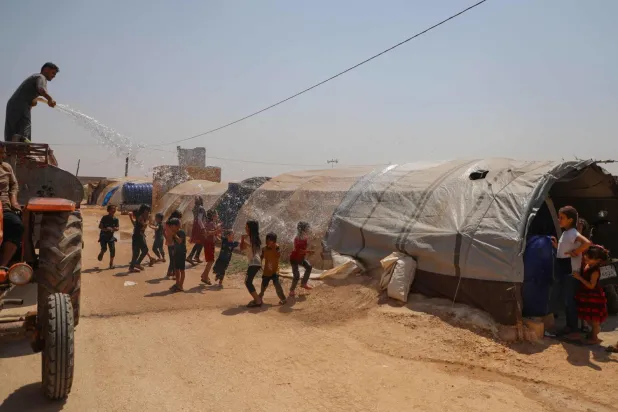 Suriye'nin kuzeybatısındaki Zerdana köyündeki bir mülteci kampında pazartesi günü yüksek sıcaklıklar nedeniyle serinlemeleri için çocukların üzerine su serpildi (AFP)