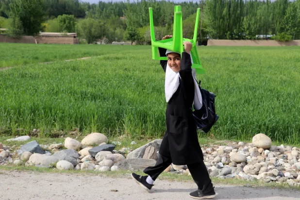 صورة أرشيفية لطالبة أفغانية تحمل كرسيها وحقيبتها الدراسية قبل حكم طالبان (أ.ف.ب)