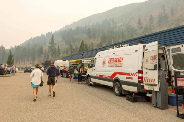 أشخاص يسيرون بالقرب من سيارة طوارئ في جيم ليند أرينا مع استمرار اندلاع حريق غابات ماكدوجال كريك في ويست كيلونا، كولومبيا البريطانية (أ.ف.ب)