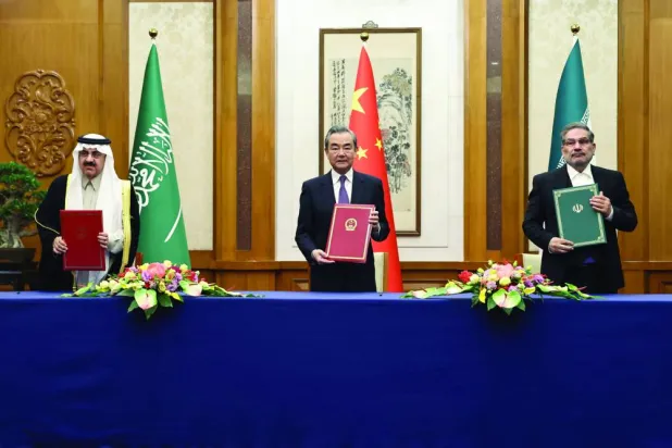 وزير الخارجية الصيني وانغ يي متوسطاً رئيسي الوفدين المفاوضين السعودي الدكتور مساعد العيبان والإيراني علي شمخاني بعد توقيع وثيقة الاتفاق في 10 مارس الماضي (رويترز)