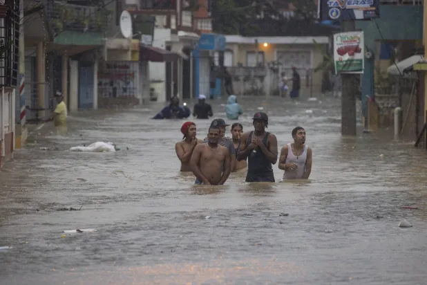 أشخاص يسيرون في شارع غمرته المياه بعد مرور العاصفة الاستوائية «فرانكلين» في سانتو دومينغو  (إ.ب.أ)