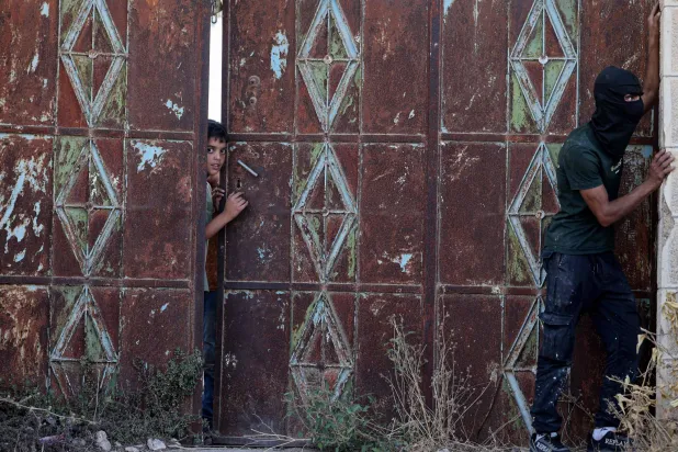 ایک لڑکا گیٹ کے پیچھے سے جھانک رہا ہے جب کہ اسرائیلی فوجی پیر کے روز مغربی کنارے کے گاؤں بیتا میں تلاشی مہم چلا رہے ہیں (اے ایف پی)