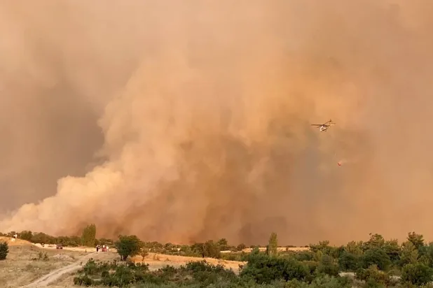 طائرة هليكوبتر تحلق وسط الدخان الناجم عن حرائق الغابات في كاناكالي بتركيا (رويترز)