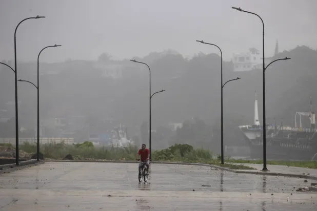 رجل يركب دراجته تحت المطر الناجم عن مرور العاصفة الاستوائية فرانكلين في سانتو دومينغو (إ.ب.أ)