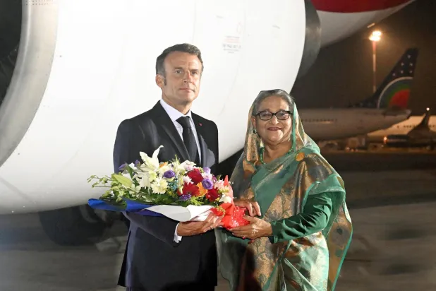 شيخة حسينة لدى استقبالها إيمانويل ماكرون في مطار دكا أمس (إ.ب.أ)