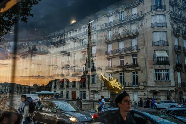 انعكاس برج إيفل يظهر عند غروب الشمس بينما يسير المشاة أمام محطة للحافلات في باريس (أ.ف.ب)