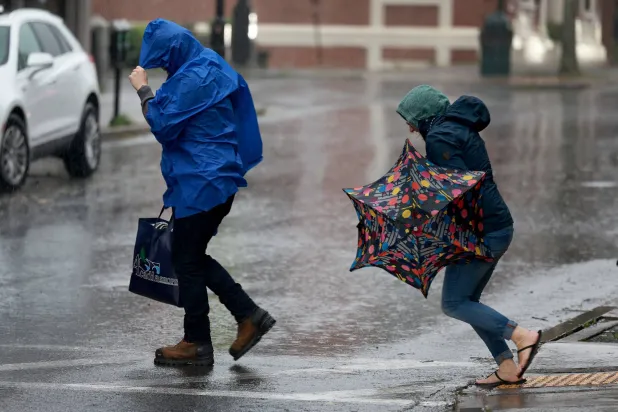 أميركيون يعبرون الطريق وسط الرياح والأمطار من إعصار «لي» في ولاية «مين» (أ.ف.ب)