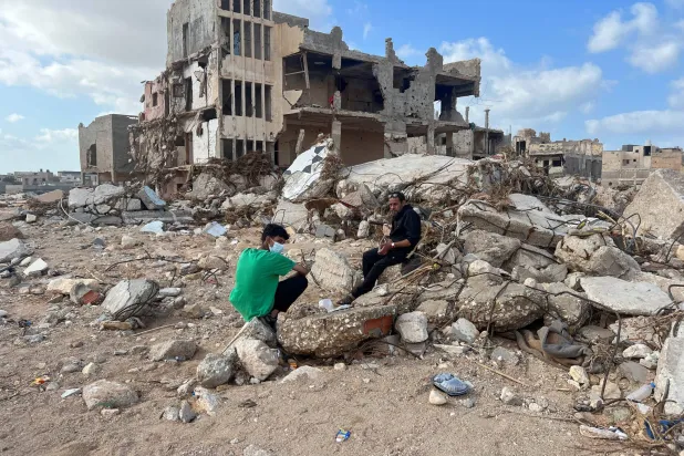 مواطنان يجلسان أمام بقايا منزل تهدم في مدينة درنة الليبية (رويترز)