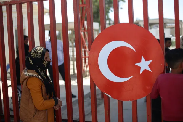 مهاجرة تطلّ من سياج حدودي مع سوريا في شانلي أورفا، مايو 2023 (غيتي)