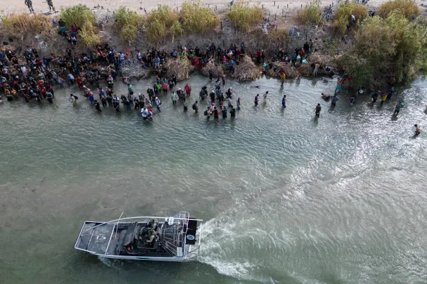 صورة جوية تظهر قارباً لحرس الحدود الأميركي يمر بمجموعة كبيرة من المهاجرين الذين ينتظرون عبور حاجز الأسلاك الشائكة إلى الولايات المتحدة في إيغل باس بولاية تكساس في 25 سبتمبر 2023 (أ.ف.ب)