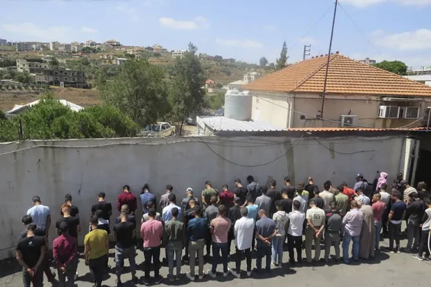 In this photo released on Aug. 9, 2023, by the Lebanese Army official website, the Lebanese Army lines up a group of Syrians accused of illegally crossing into Lebanon from Syria by way of smugglers in the town of Shadra, northern Lebanon's Akkar province. (Lebanese Army Website via AP) 