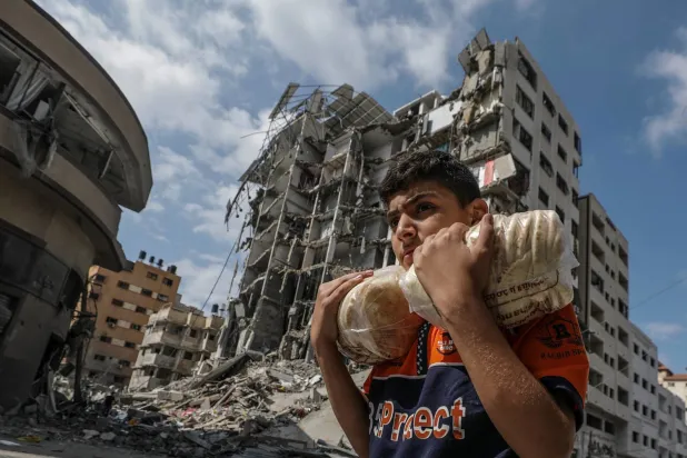 Gazze’de dün İsrail saldırısında yıkılan bir binanın önünden elinde ekmekle geçen Filistinli bir genç (EPA)