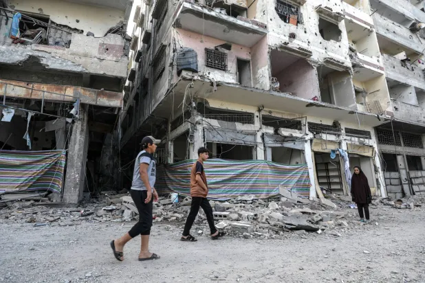 فلسطينيون يسيرون بجوار المباني التي دمرتها الغارات الإسرائيلية الأخيرة في شرق مدينة غزة (إ.ب.أ)