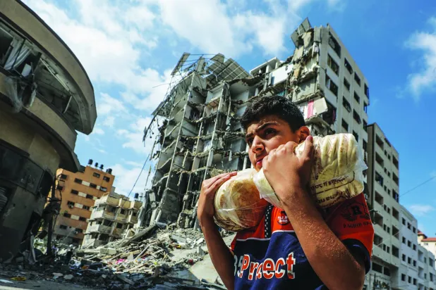 غزہ شہر میں ایک فلسطینی لڑکا روٹیاں لیے ایک عمارت کے سامنے سے گزر رہا ہے جو کل اسرائیلی حملے سے تباہ ہو گئی تھی (اے پی)