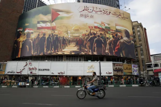 رجل إيراني يقود سيارته بجوار لوحة إعلانية ضخمة مؤيدة للفلسطينيين معلقة في ساحة ولي عصر في طهران إيران 25 أكتوبر 2023 (إ.ب.أ)