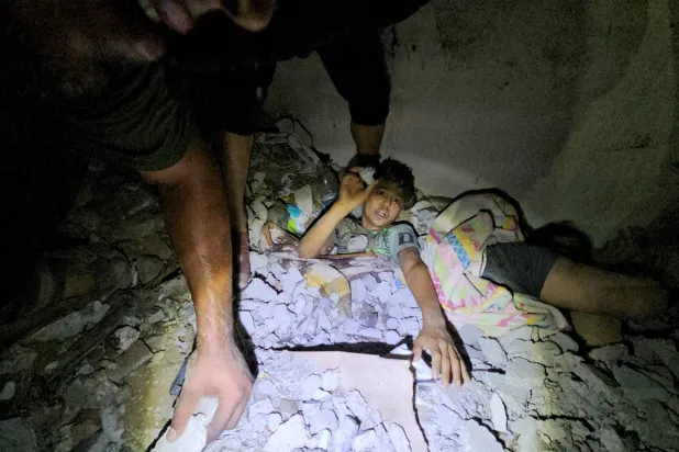 فلسطينيون يعملون على إنقاذ صبي محاصر تحت الأنقاض بعد غارة إسرائيلية على منزل في جباليا شمال قطاع غزة (رويترز)