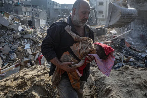 فلسطيني يحمل طفلاً انتُشل من تحت أنقاض مخيم جباليا للاجئين بعد يوم واحد من غارة جوية على المنطقة في شمال غزة (إ.ب.أ)