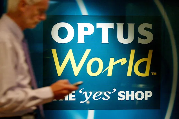 رجل يتحقق من هاتفه الجوال وهو يمشي بالقرب من لافتة لـ«أوبتوس» في سيدني (أ.ف.ب)