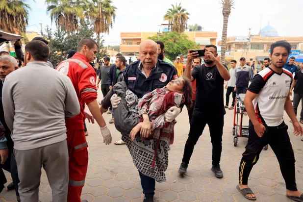 رجل ينقل فتاة فلسطينية مصابة إلى مستشفى الأقصى عقب القصف الإسرائيلي على دير البلح (أ.ف.ب)