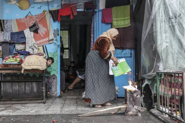 فلسطينية نزحت بسبب القصف الإسرائيلي تشعل النار للطهي في مدرسة تديرها الأمم المتحدة في مدينة غزة الاثنين في اليوم الرابع (أ.ب)