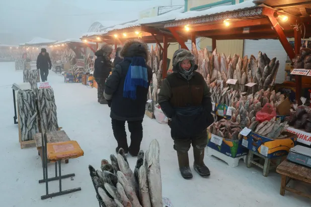 بائع يقف بجوار الأسماك المجمدة في سوق بالهواء الطلق وسط يوم بارد في ياكوتسك (رويترز)