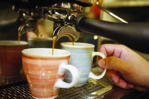 رجل يحضِّر فنجانين من القهوة بمقهى في كولومبيا (إ.ب.أ)