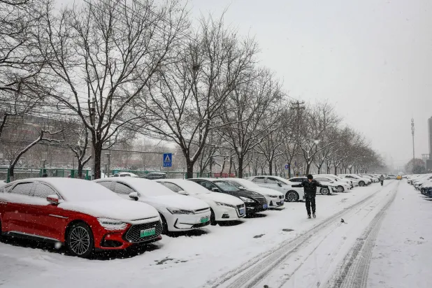 رجل يمشي بجوار السيارات المغطاة بالثلوج في بكين (إ.ب.أ)