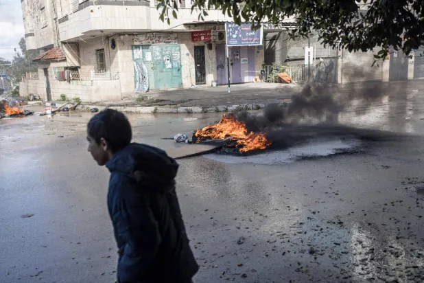 رجل يسير بجوار إطارات مشتعلة عند مدخل مخيم جنين للاجئين في جنين الأربعاء (أ.ف.ب)