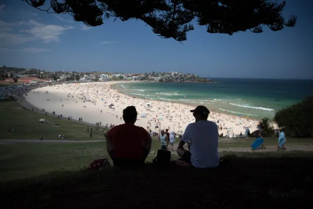 شخصان يجلسان في الظل فوق شاطئ بوندي في سيدني بأستراليا (إ.ب.أ)