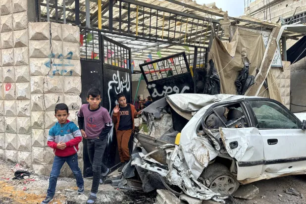 أطفال فلسطينيون يعبرون سيارة دمرها الهجوم الإسرائيلي على مخيم نور شمس (أ.ف.ب)