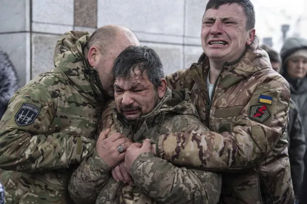 Ukrainian servicemen cry near the coffin of their comrade Andrii Trachuk during his funeral service on Independence square in Kyiv, Ukraine, Friday, Dec. 15, 2023. (AP Photo/Evgeniy Maloletka)