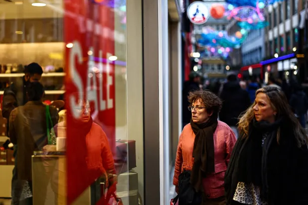 متسوقون يسيرون بجوار متجر يعرض لافتة كتب عليها «تخفيضات» في وسط لندن، ارتفع عدد المتسوقين خلال الأيام الماضي بنسبة 4 في المائة بجميع متاجر التجزئة في المملكة المتحدة (أ.ف.ب)