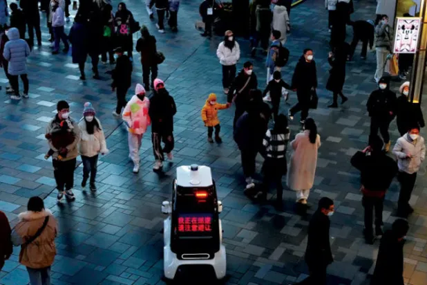 سيارة روبوتية مصنوعة في الصين تابعة للشرطة تقوم بدوريات بالقرب من حشد من الناس في بكين (أ.ب)