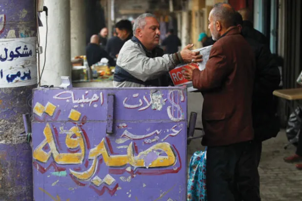صراف في أحد شوارع بغداد وهو يهم بحمل عبوة لأوراق نقدية في مشهد يعبر عن تضاؤل العملة العراقية (أ.ف.ب)