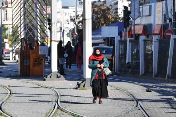 تونسية تسير فوق أحد خطوط الترام عقب تنظيم إضراب واسع بقطاع النقل في العاصمة يوم الاثنين (أ.ف.ب)