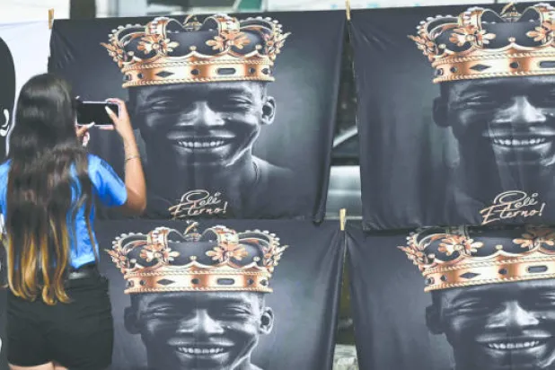 إحدى المعزيات تلتقط صورة لقطع قماش مطبوع عليها صور رمزية للراحل بيليه (أ.ف.ب)