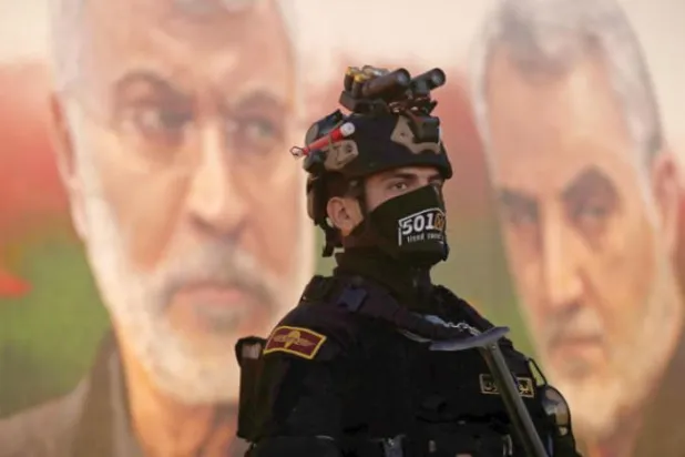 A member of Iraq’s PMF stands guard in front of a banner depicting slain Iraqi deputy chief Abu Mahdi al-Muhandis and Iranian Quds Force commander Qassem Soleimani (AFP)