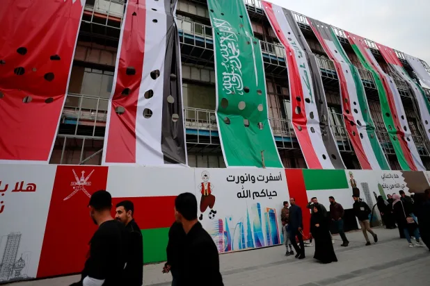 People walk in front of a building bearing flags of Arab nations on its facade, in the Al-Ashar district of Iraq's southern city of Basra on January 5, 2023, ahead of the 25th Arabian Gulf Cup football championship. (AFP)