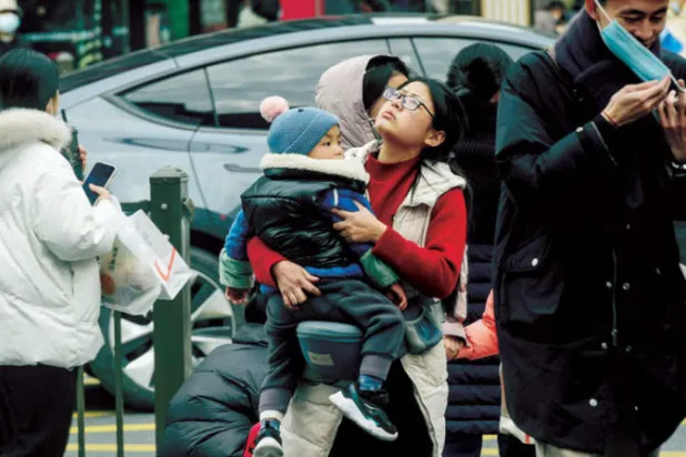 امرأة تحمل طفلاً بينما تعبر طريقاً في هانغزو شرق الصين (أ.ف.ب)