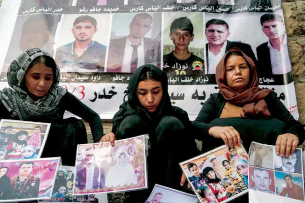 سيدات أيزيديات يعرضن صوراً لضحايا «داعش» الإرهابي (أ.ف.ب)