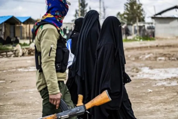 نساء في مخيم «الهول» يمشين تحت حراسة «قوات سوريا الديمقراطية» (أ.ف.ب)