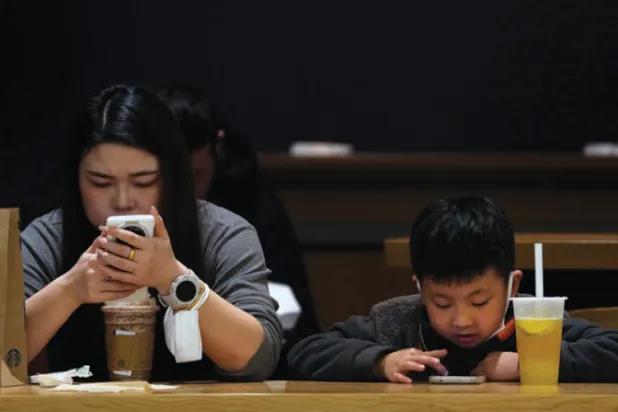 امرأة وطفل يتفحصان هاتفيهما الذكيين داخل مقهى في بكين (أ.ب)