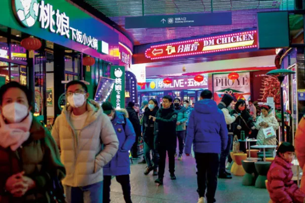 صينيون يسيرون وسط مطاعم في منطقة تجارية بالعاصمة بكين (إ.ب.أ)