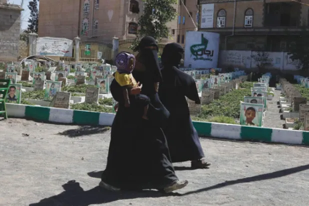 نساء يمنيات يمشين بجوار مقبرة لقتلى الحوثيين في صنعاء (إ.ب.أ)