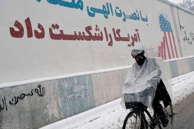 أفغاني يقود دراجة أمام لوحة جدارية خارج السفارة الأميركية المغلقة أثناء تساقط الثلوج في العاصمة كابل الخميس (أ.ف.ب)