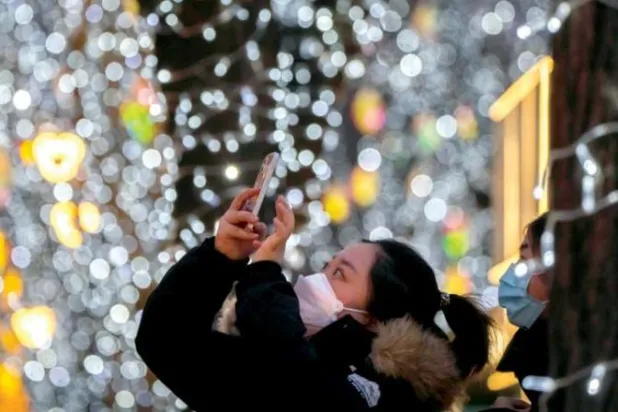 فتاة صينية تلتقط صورة للأضواء والزينات في أحد المراكز التجارية بالعاصمة بكين (أ.ب)